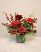 Load image into Gallery viewer, A festive floral arrangement featuring red roses, ilex, pinecones, and green foliage in a muted green vase.